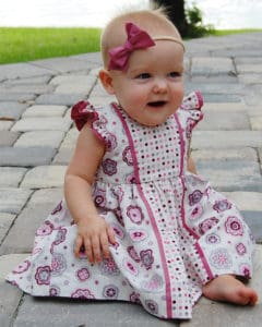Simple Life Pattern Company | Baby Geneva's Vintage Bow Dress. Downloadable PDF Sewing Pattern for Baby Sizes Newborn to 24 Months. Baby Geneva's Vintage Bow Dress is a stylish dress with the most beautiful vintage feel.  Whether you are looking for an everyday dress or something more fancy for a special occasion this pattern will be a staple in your stash.  Featuring several stunning sleeve lengths: sleeveless, single flutter sleeves double flutter sleeves, an open short sleeve or long sleeve with ties...the styling options are endless! The bodice offers two gorgeous necklines, the traditional scoop neck or a more modern square neck.  You can choose a simple bodice, bodice with a simple center panel or bodice with a pin tuck center panel. Baby Geneva includes several skirt options: a simple gathered vintage skirt, a gathered vintage skirt with center panel, a simple gathered dress skirt and a gathered dress skirt with center panel.  Vintage length is designed to fall 1” above the knee while dress length will fall at the knee. The skirt is finished off with a classic deep 1.5” hem, giving you the most stunning vintage look. The beautiful features don’t stop there.  To finish off this stunning look you have the option to add to beautiful bows to the sides of the bodice.