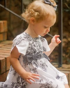 Simple Life Pattern Company | Baby Geneva's Vintage Bow Dress. Downloadable PDF Sewing Pattern for Baby Sizes Newborn to 24 Months. Baby Geneva's Vintage Bow Dress is a stylish dress with the most beautiful vintage feel.  Whether you are looking for an everyday dress or something more fancy for a special occasion this pattern will be a staple in your stash.  Featuring several stunning sleeve lengths: sleeveless, single flutter sleeves double flutter sleeves, an open short sleeve or long sleeve with ties...the styling options are endless! The bodice offers two gorgeous necklines, the traditional scoop neck or a more modern square neck.  You can choose a simple bodice, bodice with a simple center panel or bodice with a pin tuck center panel. Baby Geneva includes several skirt options: a simple gathered vintage skirt, a gathered vintage skirt with center panel, a simple gathered dress skirt and a gathered dress skirt with center panel.  Vintage length is designed to fall 1” above the knee while dress length will fall at the knee. The skirt is finished off with a classic deep 1.5” hem, giving you the most stunning vintage look. The beautiful features don’t stop there.  To finish off this stunning look you have the option to add to beautiful bows to the sides of the bodice.