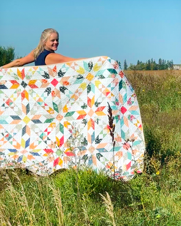 Radiant Roads Quilt Pattern by Katie Skoog for Simple Life Pattern Company featuring a stunning modern star quilt design with a classic sampler block feel. This beginner-friendly, scrappy quilt is perfect for using fat quarters or fabric scraps and features vibrant, light-filled colors on a white background. You can use a FQ bundle, jelly roll or yardage to create this simple downloadable pdf quilting pattern. Download the digital PDF quilt pattern today to create your own gorgeous handmade crib, throw, full or queen sized blanket or bed quilt. Ideal for modern quilters who love bright, fresh, and intricate-looking but simple-to-make designs. This vintage modern quilt features half square triangles HST and quick corner tulip blocks. the large 16 inch square blocks make this stunning quilt come together quick. Computer drawn line drawings and images for easy to follow step by step instructions. Fabrics from Sharon Holland for Art Gallery Fabrics. Spring summer fall autumn and winter lap quilt. Modern with a scrappy retro vibe blanket. Scrap friendly star quilt in multiple sizes.